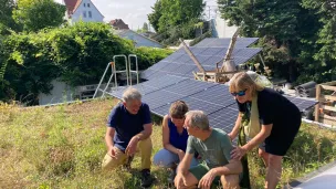 Leute sitzen auf einem Gründach vor einer Photovoltaikanlage