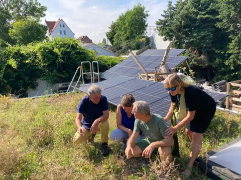Leute sitzen auf einem Gründach vor einer Photovoltaikanlage